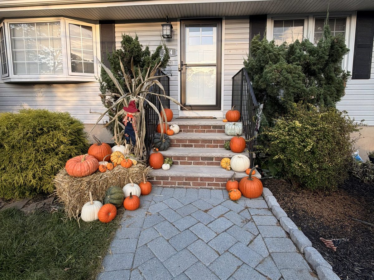Pumpkin porch display in Hillsdale, NJ: pumpkins up brick steps with a straw bale, cornstalks, and a scarecrow
