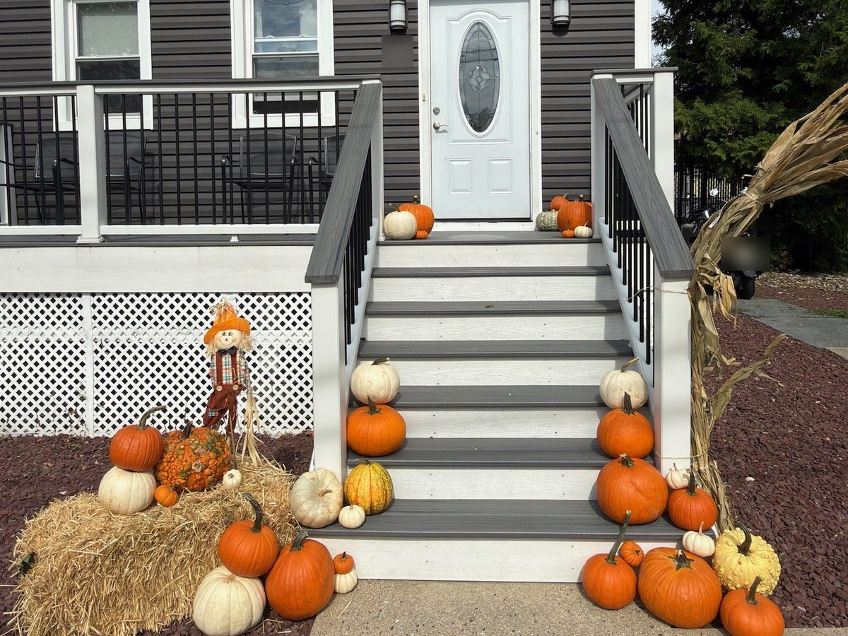 Pumpkin porch display in Hackensack, NJ: gray steps lined with pumpkins, a straw bale, and a scarecrow